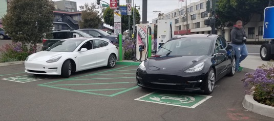 auto elektromobily Tesla Model 3 bílá černá u nabíjecí stanice Tesla Supercharger