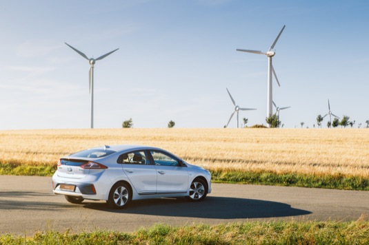 auto elektromobil Hyundai Ioniq Electric, v pozadí větrné elektrárny turbíny