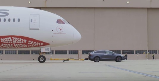 auto elektromobil Tesla Model X táhne po letištní pojezdové dráze letadlo Boeing 787-9 Dreamliner