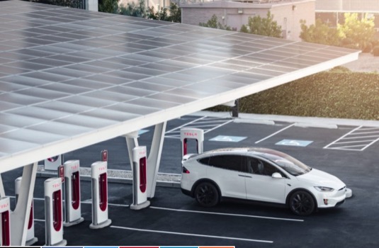 auto elektromobil Tesla Model X se nabíjí u nabíjecí stanice Tesla Supercharger doplněné o solární střešní elektrárnu